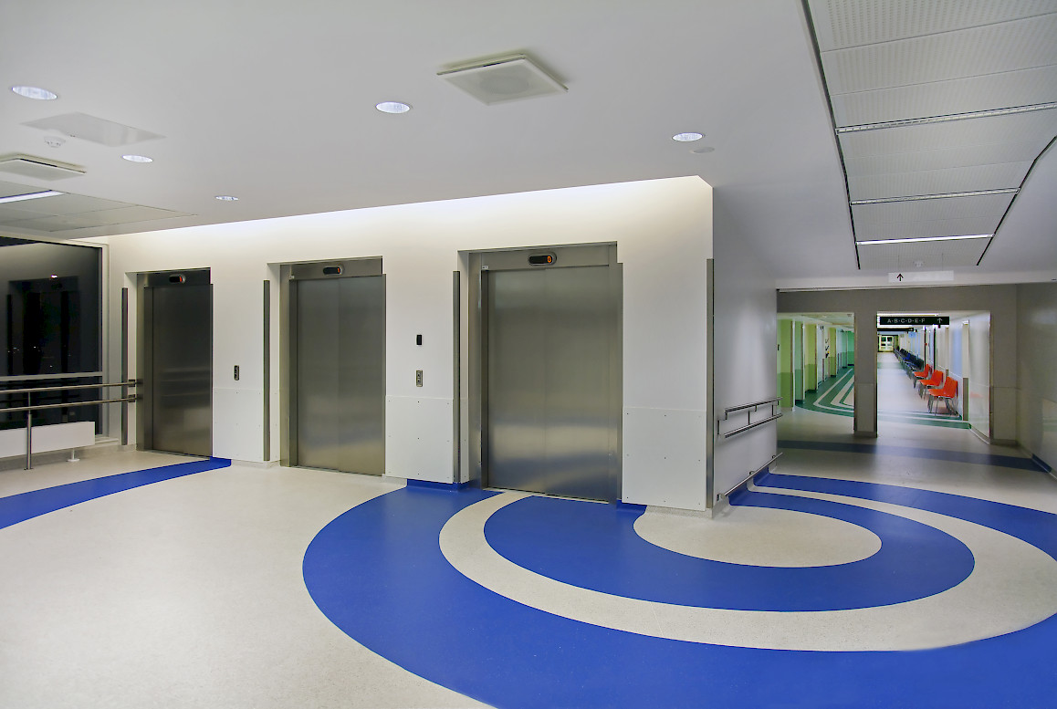 A colorful hospital entrance with some chairs and lifts.